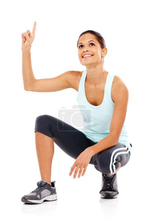 Photo for Moving up in the fitness world. An attractive young woman in gymwear crouching down and pointing upwards - Royalty Free Image