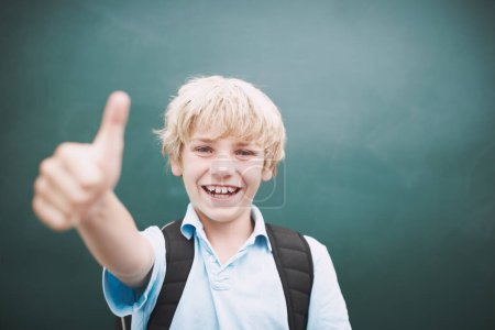 Photo for I love learning. A young boy giving you a thumbs up against a blackboard in his classroom - Royalty Free Image