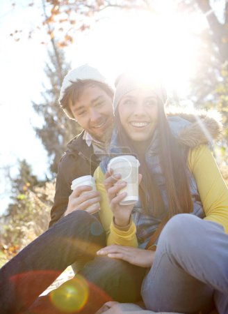Téléchargez les photos : Une partie de leur routine week-end café dans le parc. Un jeune couple affectueux assis ensemble tout en dégustant un café en plein air - en image libre de droit