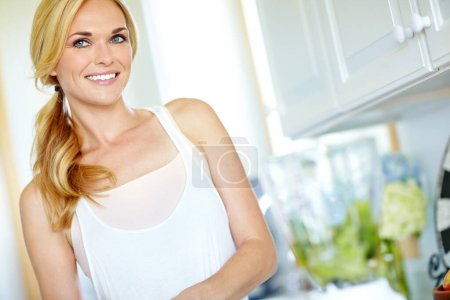 Téléchargez les photos : Elle aime être dans sa cuisine. Belle femme blonde souriante dans sa cuisine à la maison - en image libre de droit
