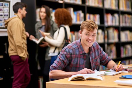 Téléchargez les photos : Étudier n'est pas aussi nul qu'échouer. un étudiant masculin étudiant dans une bibliothèque universitaire avec ses pairs en arrière-plan - en image libre de droit
