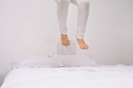 Téléchargez les photos : À quelle hauteur pouvez-vous aller ? les jambes d'une petite fille sautant sur le lit - en image libre de droit