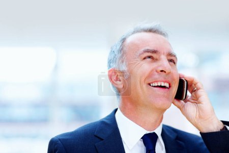 Foto de Empresario conversando por celular. Ejecutivo sonriendo y mirando hacia arriba mientras habla en el teléfono celular - Imagen libre de derechos