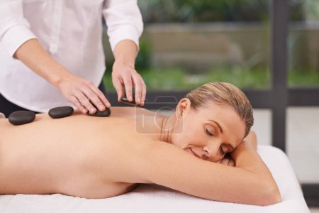 Téléchargez les photos : Les pierres chaudes sont le moyen idéal pour se détendre. une femme dans un spa de jour relaxant sur une table de massage - en image libre de droit
