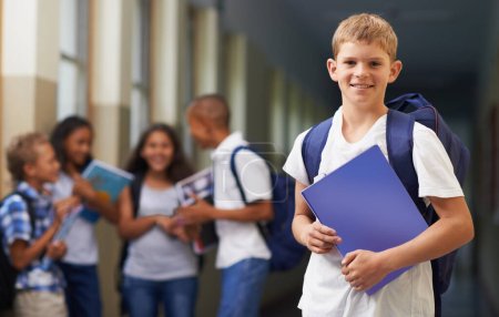 Téléchargez les photos : Prêt pour l'école. Portrait d'un garçon d'école heureux debout dans le couloir avec ses amis en arrière-plan - en image libre de droit