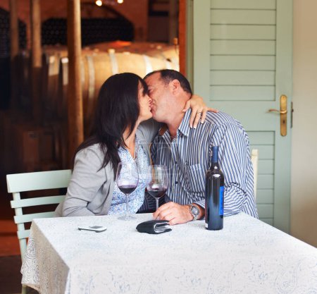 Photo for Love, kiss and a couple on a wine farm together in celebration of love or their anniversary. Kissing, romance or dating with a loving man and woman at a table in a winery feeling happy while bonding. - Royalty Free Image