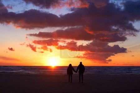 Photo for Silhouette, couple holding hands at sunset and on beach walking together. Love or care, holiday or vacation and shadows of people on the seashore for embrace for romance date or honeymoon outdoor. - Royalty Free Image