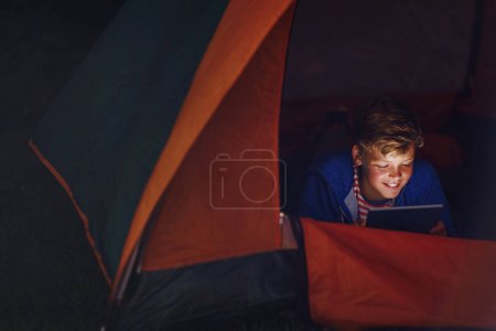 Foto de Trajo algo de entretenimiento al campamento. un niño usando una tableta digital mientras acampaba - Imagen libre de derechos