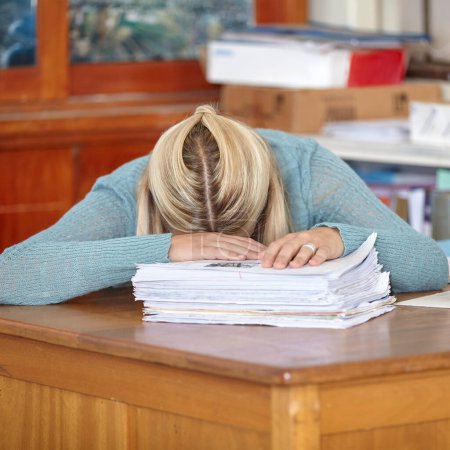Photo for She finally managed to mark all those tests. A tired teacher sitting at her classroom desk with classwork and tests to mark in front of her - Royalty Free Image
