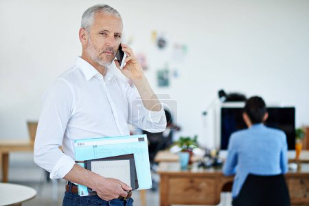 Photo for Im headed out. a mature businessman talking on a cellphone while standing in an office - Royalty Free Image