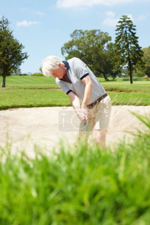 Photo for Trying to escape the sand trap. Senior man trying to hit his ball out of the sandtrap on the golf course - Royalty Free Image