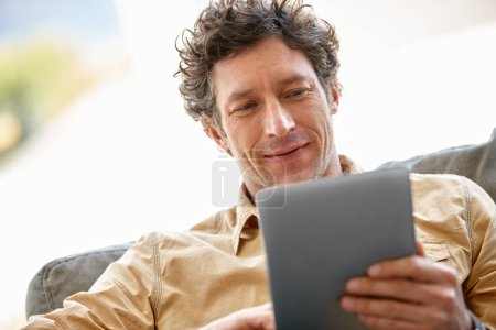 Téléchargez les photos : Loisirs en ligne. un homme mûr utilisant une tablette numérique sur le canapé à la maison - en image libre de droit