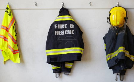 Photo for Fireman, uniform and clothing hanging on wall rack at station for fire fighting protection. Firefighter gear, rescue jacket and helmet with reflector for emergency services, equipment or department. - Royalty Free Image