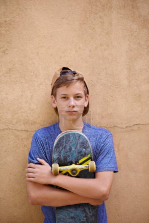 Téléchargez les photos : Skateboard proche de son cœur. Portrait d'un adolescent tenant son skateboard debout contre un mur - en image libre de droit
