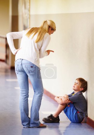 Photo for Teacher, student and scolding child at school for bad behaviour, problem or attitude. Angry woman pointing and talking to punish naughty boy for discipline, lesson or education fail in hallway. - Royalty Free Image