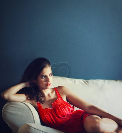 Téléchargez les photos : Rayonnant en rouge. Une belle jeune femme allongée sur le canapé avec une expression réfléchie - en image libre de droit