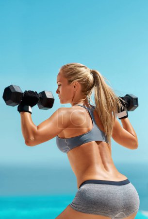 Photo for Getting her pump on. a beautiful young woman exercising with dumbbells outdoors - Royalty Free Image
