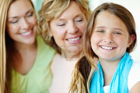 Photo for Her big smile tells you just how happy she is. A cute young girl smiling with her mother and grandmother blurred in the background - Royalty Free Image