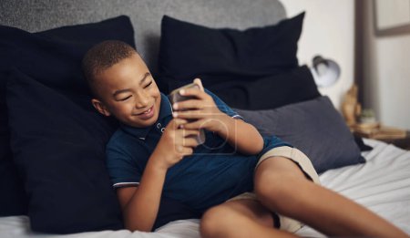 Photo for I can play lots and lots of different games on here. a young boy using a cellphone while lying on his bed - Royalty Free Image