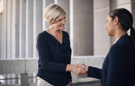 Foto de Reunirnos por el bien del negocio. dos mujeres de negocios estrechando la mano contra un fondo de la ciudad - Imagen libre de derechos