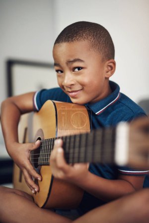 Téléchargez les photos : Jouer de la guitare me rend encore plus cool. un jeune garçon jouant de la guitare à la maison - en image libre de droit