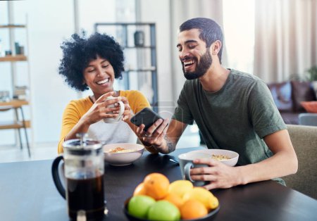Foto de Es el influencer más gracioso que conozco. una pareja joven mirando algo en un teléfono móvil mientras desayuna en casa - Imagen libre de derechos