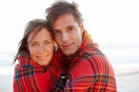 Foto de Envuelto en afecto. Una pareja devota y cariñosa envuelta en una manta en la playa - Imagen libre de derechos