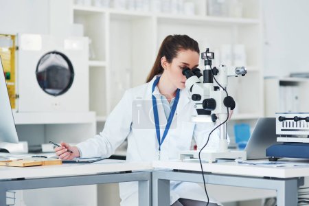Photo for I see something has changed. a focused young female scientist looking through a microscope and making notes inside of a laboratory - Royalty Free Image