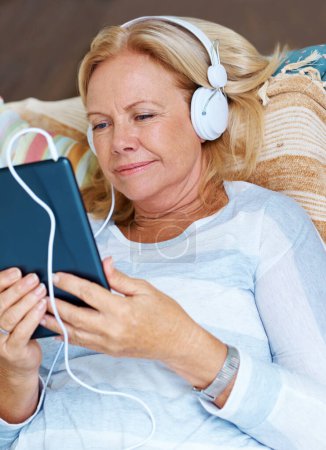 Foto de Soapies en movimiento. Una mujer mayor mirando su tableta digital mientras usa auriculares - Imagen libre de derechos