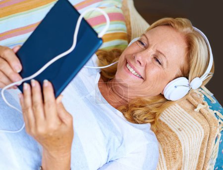 Photo for Staying updated with all the latest movies. a senior woman enjoying herself while looking at the screen and wearing headphones - Royalty Free Image
