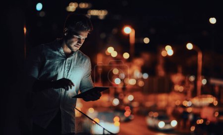 Photo for Maintaining 247 connectivity with success. a young businessman using a digital tablet outside an office at night - Royalty Free Image