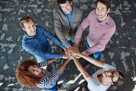 Photo for We owe it all to teamwork. High angle portrait of a group of smiling coworkers standing in hand in hand in a huddle in an office - Royalty Free Image