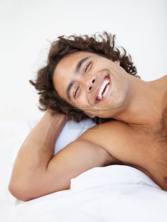 Photo for Face, laugh and a handsome man in bed in his home to relax or rest alone on a summer morning. Smile, wellness and lifestyle with a happy young male person relaxing in the bedroom of his house. - Royalty Free Image
