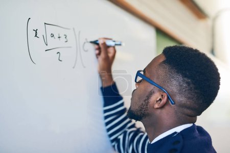Téléchargez les photos : Il peut résoudre n'importe quoi. un jeune homme écrivant sur un tableau blanc dans une classe - en image libre de droit