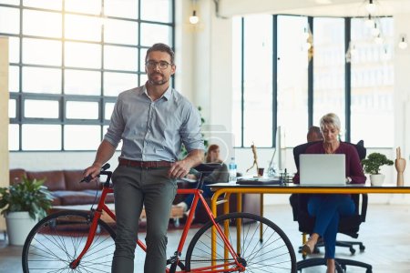Photo for We prefer keeping our workspace casual and free. Portrait of a mature designer standing in an office with his bicycle - Royalty Free Image