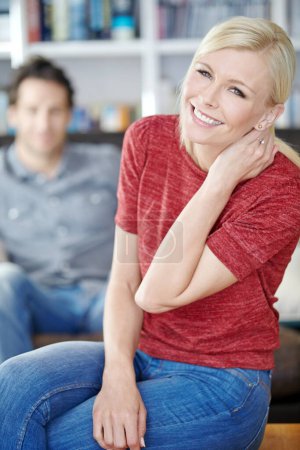 Photo for Relaxed and calm at home. Portrait of an attractive young woman sitting in a living room with her boyfriend in the background - Royalty Free Image