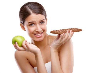 Photo for I know which one I want, but...Studio portrait of a young woman having to choose between chocolate and an apple - Royalty Free Image