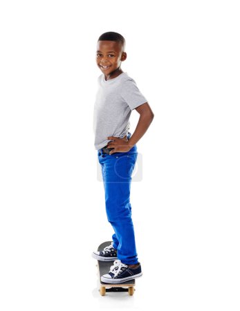 Téléchargez les photos : Pourquoi marcher quand on sait patiner ? Studio plan d'un petit garçon mignon posant avec son skateboard sur un fond blanc - en image libre de droit