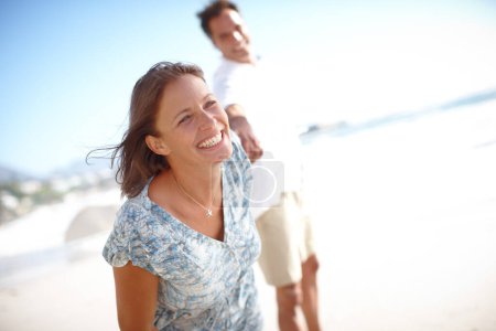 Téléchargez les photos : Où qu'elle aille, il suivra toujours. Portrait d'une femme mûre heureuse conduisant son mari par la main tout en marchant sur la plage ensemble - en image libre de droit