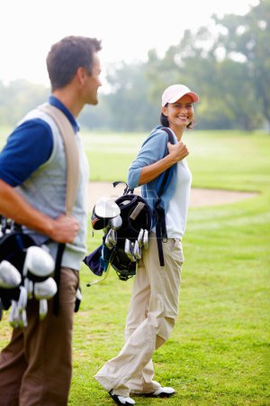 Téléchargez les photos : Une femme portant un sac de golf. Focus sur une femme souriante portant un sac de golf et regardant l'homme - en image libre de droit