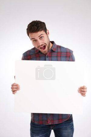 Photo for Its crazy, but its true. Studio shot of a young man holding a blank white poster looking really excited - Royalty Free Image