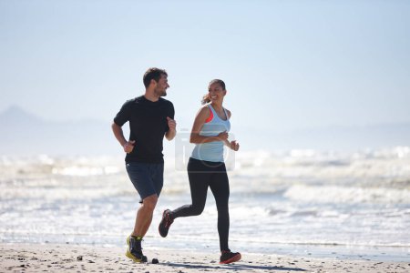 Foto de Nos mantenemos motivados. De cuerpo entero de una joven pareja corriendo a lo largo de una playa juntos - Imagen libre de derechos