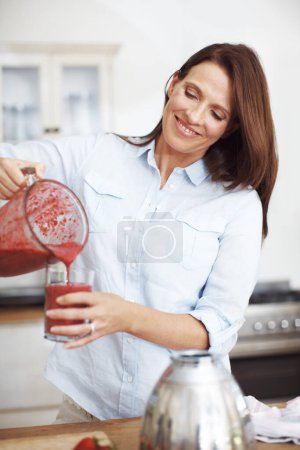 Foto de Encantador desayuno licuado. Una atractiva mujer vertiendo fruta mezclada en un vaso mientras está de pie en un mostrador de cocina - Imagen libre de derechos