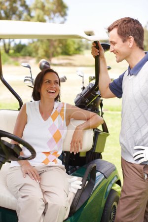Foto de Amor y risas en el green. Mujer sonriente sentada en un carrito de golf con su marido de pie junto a ella - Imagen libre de derechos