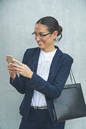 Photo for So many useful apps for business. a young businesswoman using her phone while standing against a gray wall - Royalty Free Image