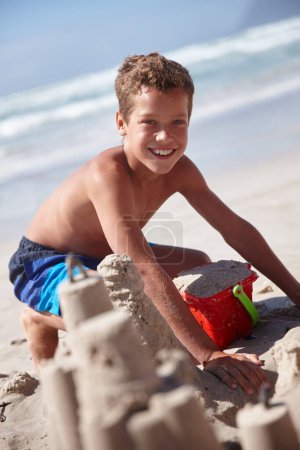 Téléchargez les photos : Les châteaux de sable sont ce dont les rêves d'enfance sont faits. un mignon petit garçon construisant un château de sable à la plage - en image libre de droit