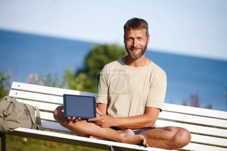 Foto de Reglas por las que vivir. un hombre maduro sosteniendo una tableta digital mientras está sentado en un banco al aire libre - Imagen libre de derechos