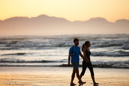 Téléchargez les photos : C'est l'heure de commencer la journée. un couple marchant le long d'une plage à l'aube - en image libre de droit