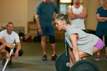 Photo for I will not be stopped. a woman lifting weights while a group of people in the background watch on - Royalty Free Image
