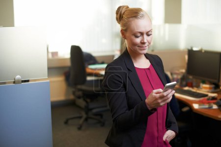 Foto de Comprobando un mensaje de su cliente. una atractiva mujer de negocios usando su celular en la oficina - Imagen libre de derechos